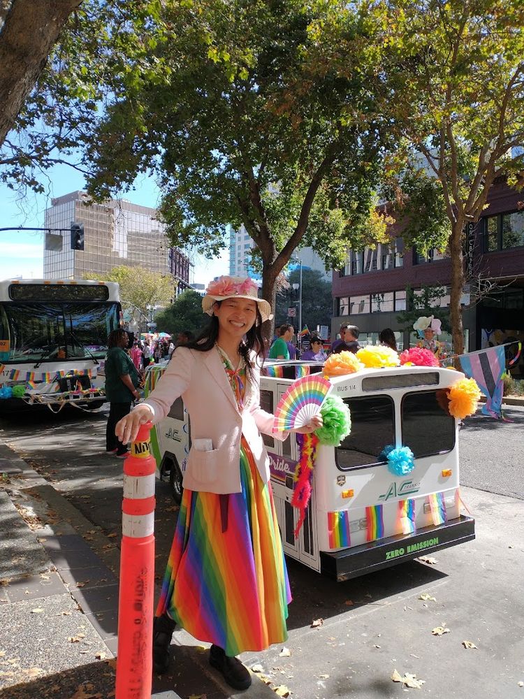 Alfred wearing a rainbow dress in front of smol bus