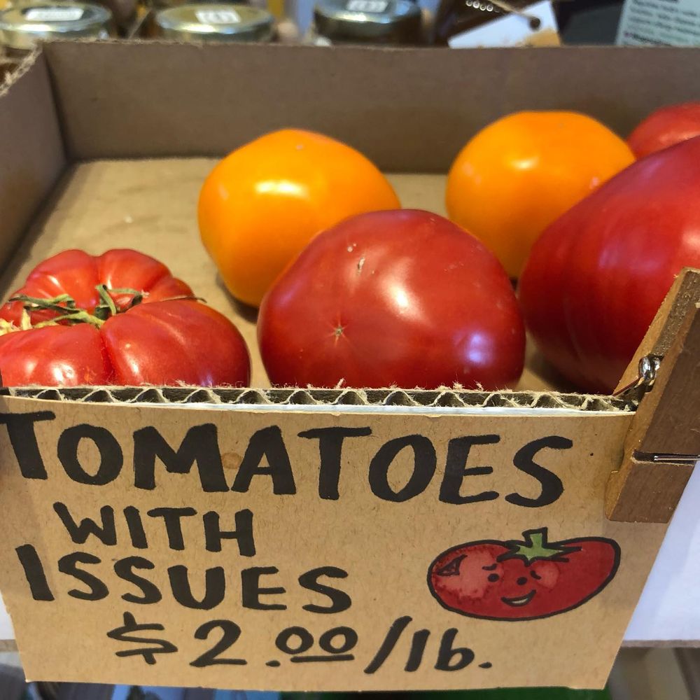 Cardboard box containing four red and two yellow tomatoes with wording, "Tomatoes with Issues $2.00 a pound."