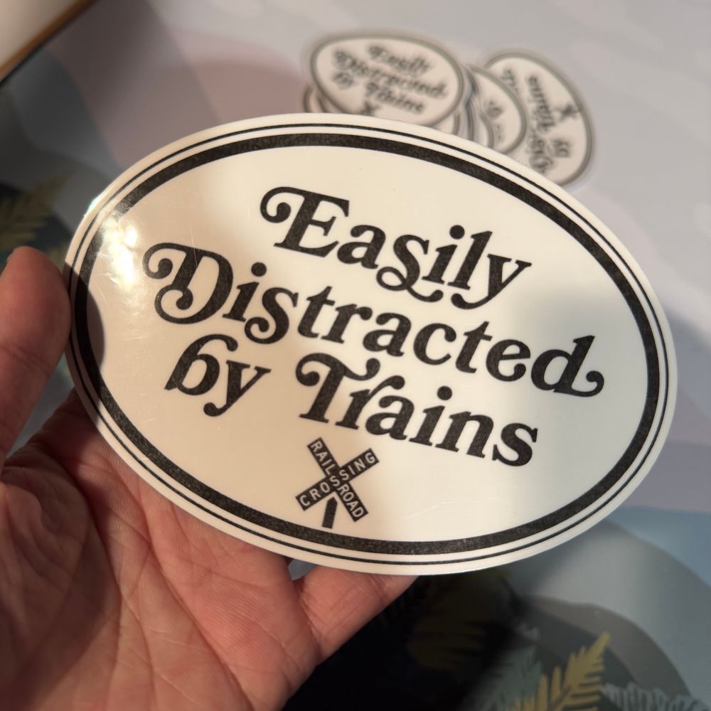 Glossy white magnet that says “easily distracted by trains” next to an icon of a railroad crossing