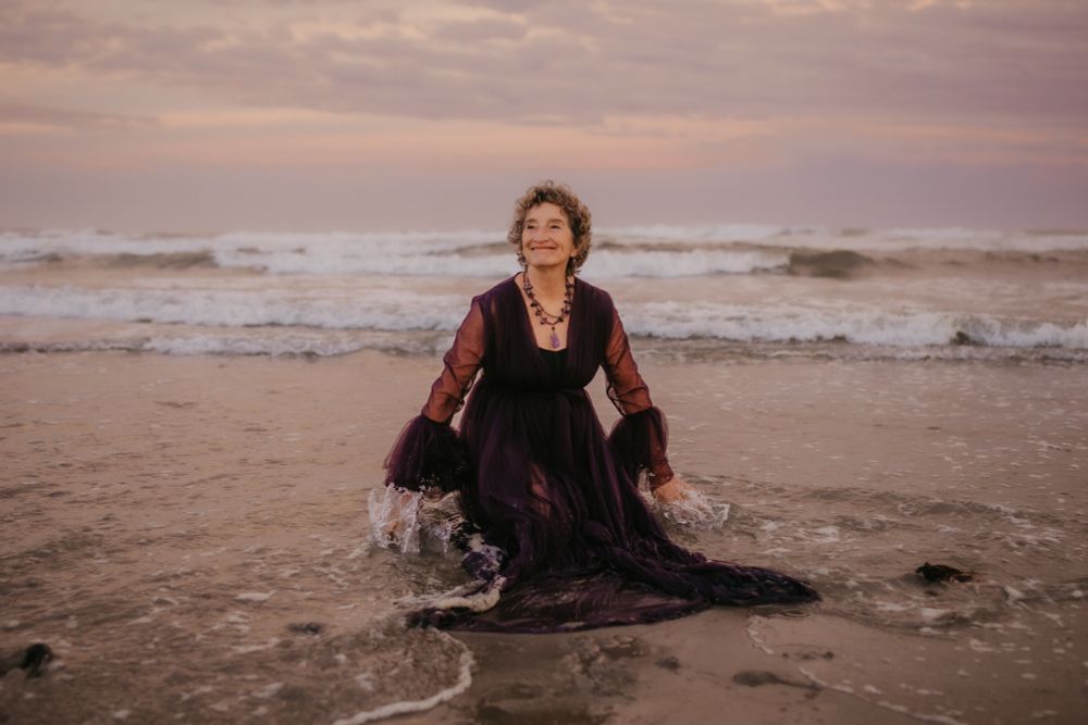 A women kneeling in shallow waves, in a dark purple gown