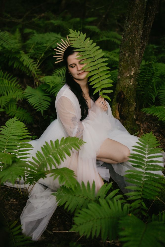 A woman in a white tulle gown, surrounded by large green ferns