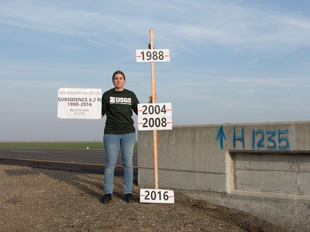 Photo of hydrologist Michelle Sneed holding a pole marking changes in land surface elevation at a location in California between 1988 and 2016. 