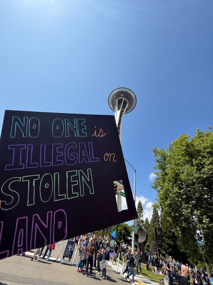 My sign, which reads “No one is illegal on stolen land,” in front of the Space Needle.