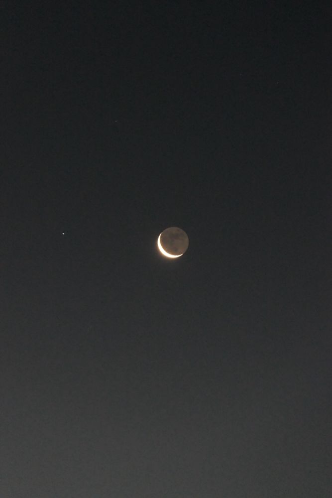 A black night sky, around 06.30 GMT, showing the waning crescent moon and the tiny white dot of Spica, in the constellation of Virgo, to the left of it. 
