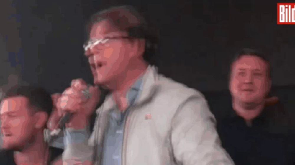 a man singing into a microphone with the word bild on the bottom left