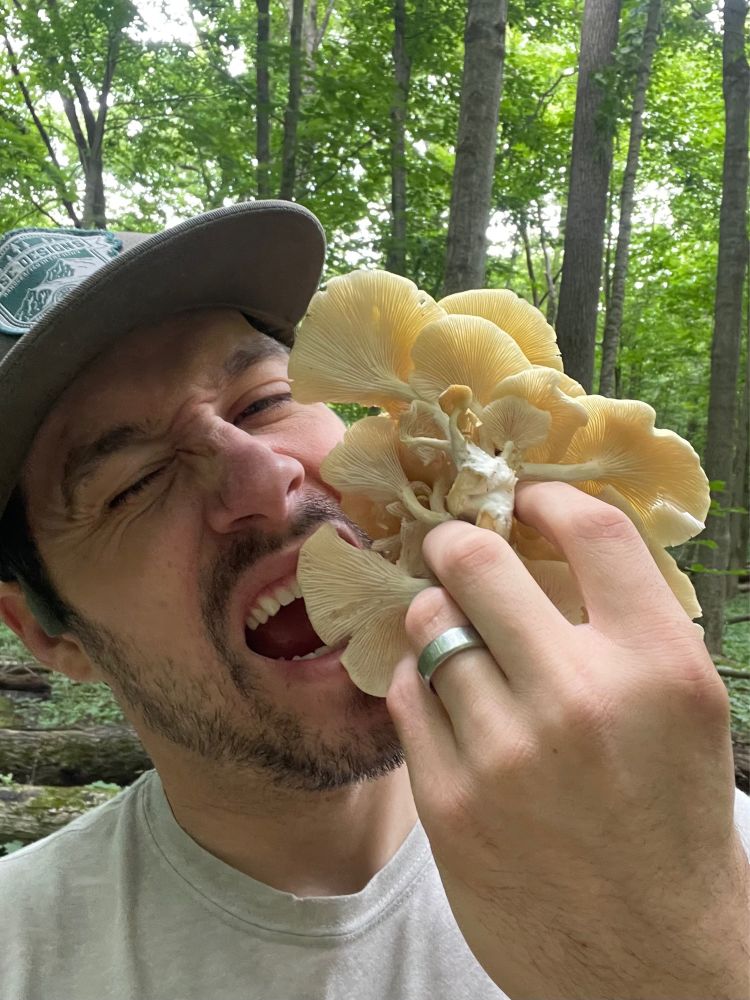 A white man (me) pretends to take a bite out of a cluster of fresh oyster mushrooms in the woods