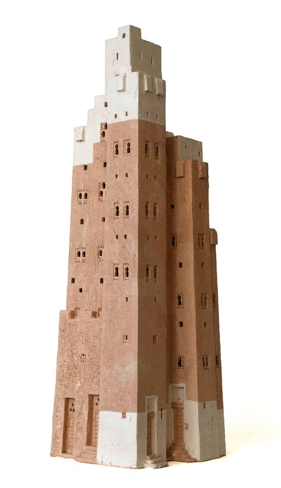 maqueta de cerámica de un edificio compuesto por diversas torres unidas formando una estructura de diversas altura ligeramente piramidal. En la base algunos de los cuerpos están pintados de blanco. hay puertas muy estilizadas detrás de unos cuantos escalones. El cuerpo del edificio está en color arcilla y presenta pequeñas ventanas agrupadas de dos en dos de estilo morisco. El remate tiene diferentes alturas y está pintado de blanco. Con pequeñas ventanas cuadradas sin decoración y volúmenes apenas sobresalientes de la fachada.