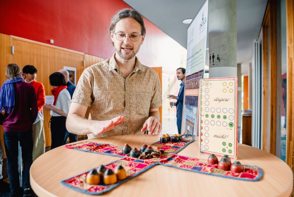 Jacob Schmidt-Madsen in the lobby of the Institute during an event. He demonstrates an Asian board game opposed to the German board game “Mensch ärgere dich nicht” („Man, Don’t Get Angry“). Photo: Sandra Prengel, 2024.