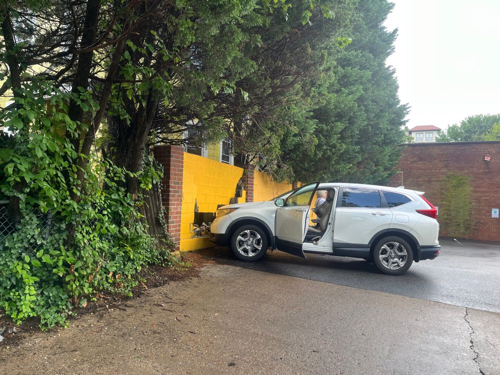 White SUV with front end against yellow cinder block wall that’s collapsing from collision. In a parking & goodness knows how in the Sam hell the driver did this.