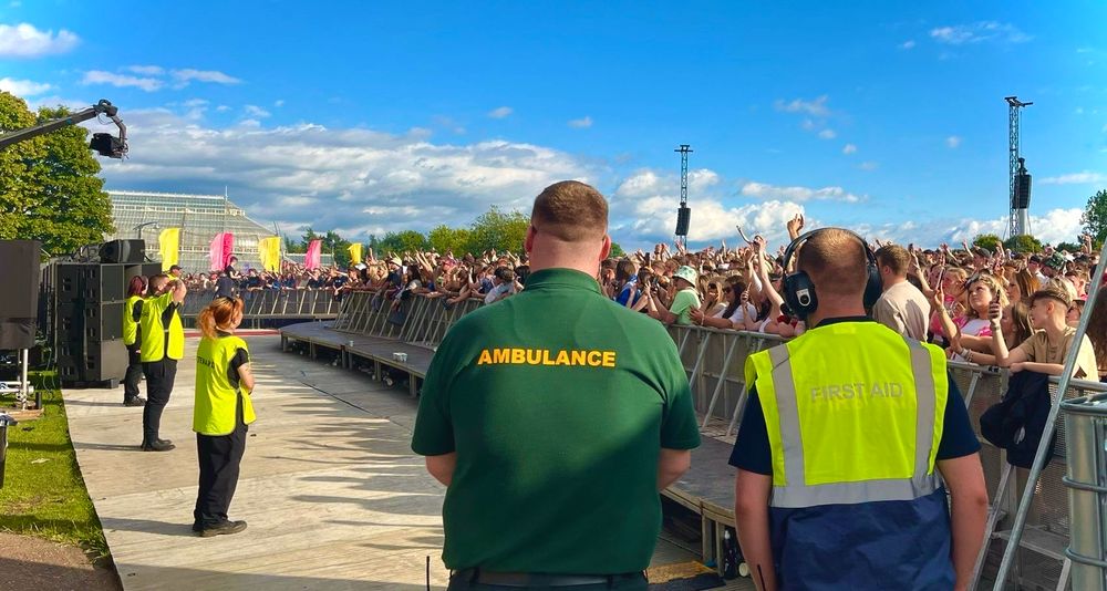 Ambulance and First Aid staff working in the front of stage pit at Scottish musical festival TRNSMT, while stewarding colleagues watch over the thousands of spectators enjoying live music in the sun.