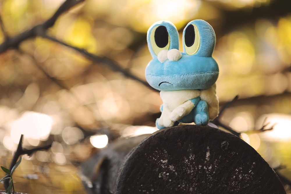 2013 Froakie Pokémon Doll sitting on top of a log that has fallen into a body of water