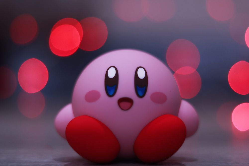 Kirby Nendoroid from Good Smile Company sitting on a wooden floor against a pink background 