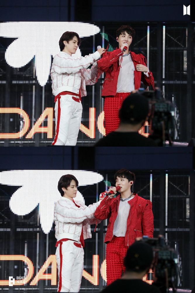 Jimin and j-hope on stage in the red and white costumes from PTD concerts. Jimin seems to be fixing something on j-hope's shoulder while j-hope is speaking