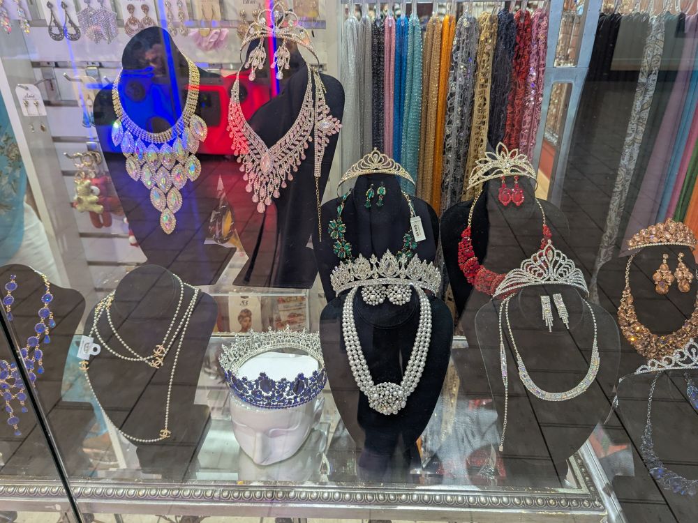 Photo through a glass window of a variety of tiaras and glittering necklaces.
