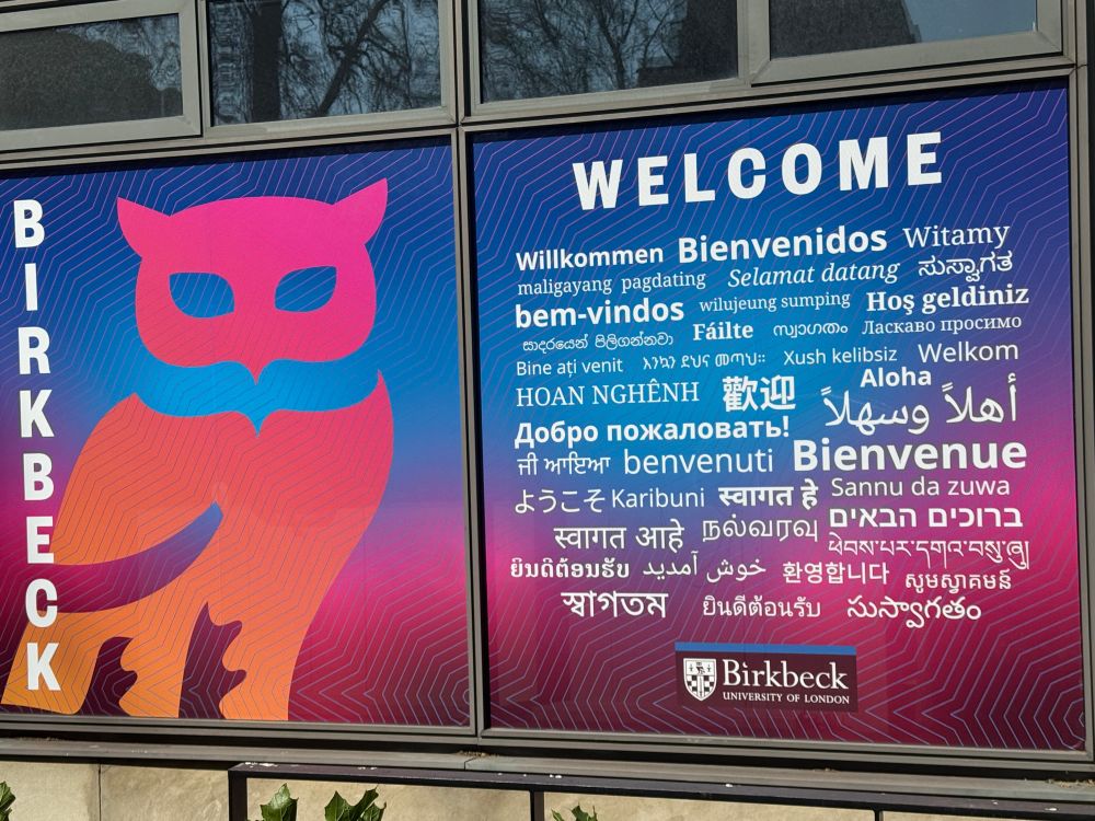 Sign at Birkbeck College with ‘welcome’ in 40-50 global languages. The symbol on one side of the sign is a stylised owl because they specialise in evening classes. 