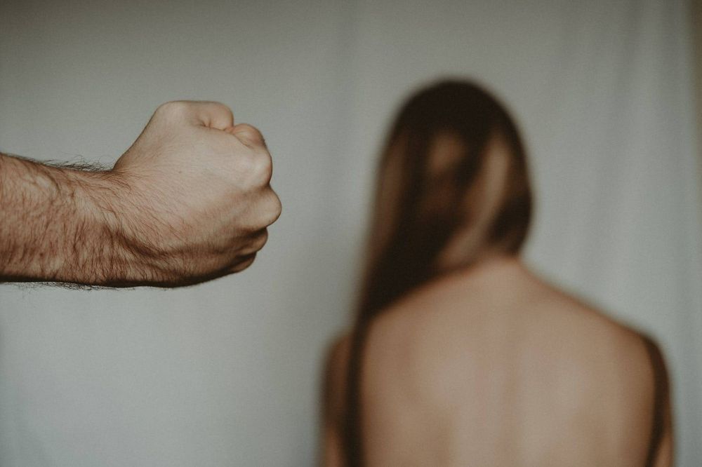 Im Hintergrund, abgewandt, langhaarige Personmit nacktem Rücken. Im Vordergrund geballte Faust an behaartem Arm