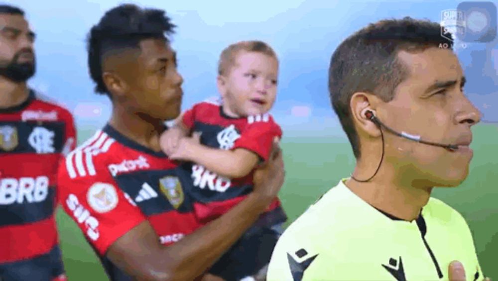 a soccer player holds a baby in front of a referee who is wearing headphones