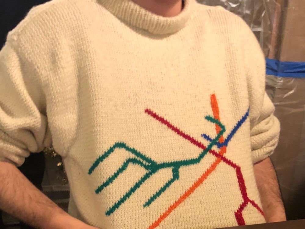 Person showing off the sweater they made: white with the MBTA system map knitted into it