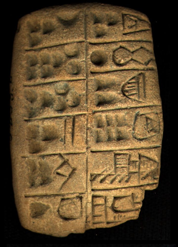 Photo of a clay tablet with round shapes impressed into is and traced drawings of objects separated into boxes