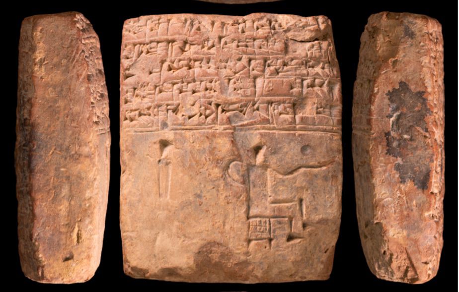 Photo of a square shaped clay tablet with 5 lines cuneiform text followed by a ruling (a line). In the blank space below the line, the student has drawn a seated figure with an outstretched arm and possibly the start of another figure behind that one. 