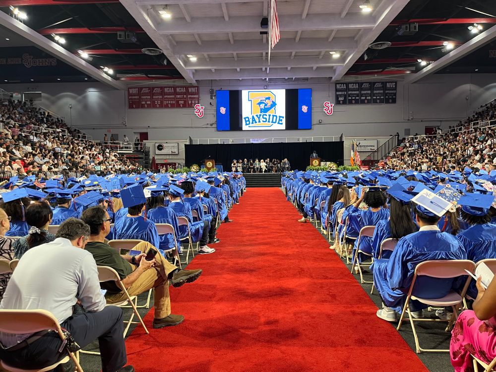 Graduating class of Bayside HS in blue caps and gowns listening to a speaker at Carnesecca Arena