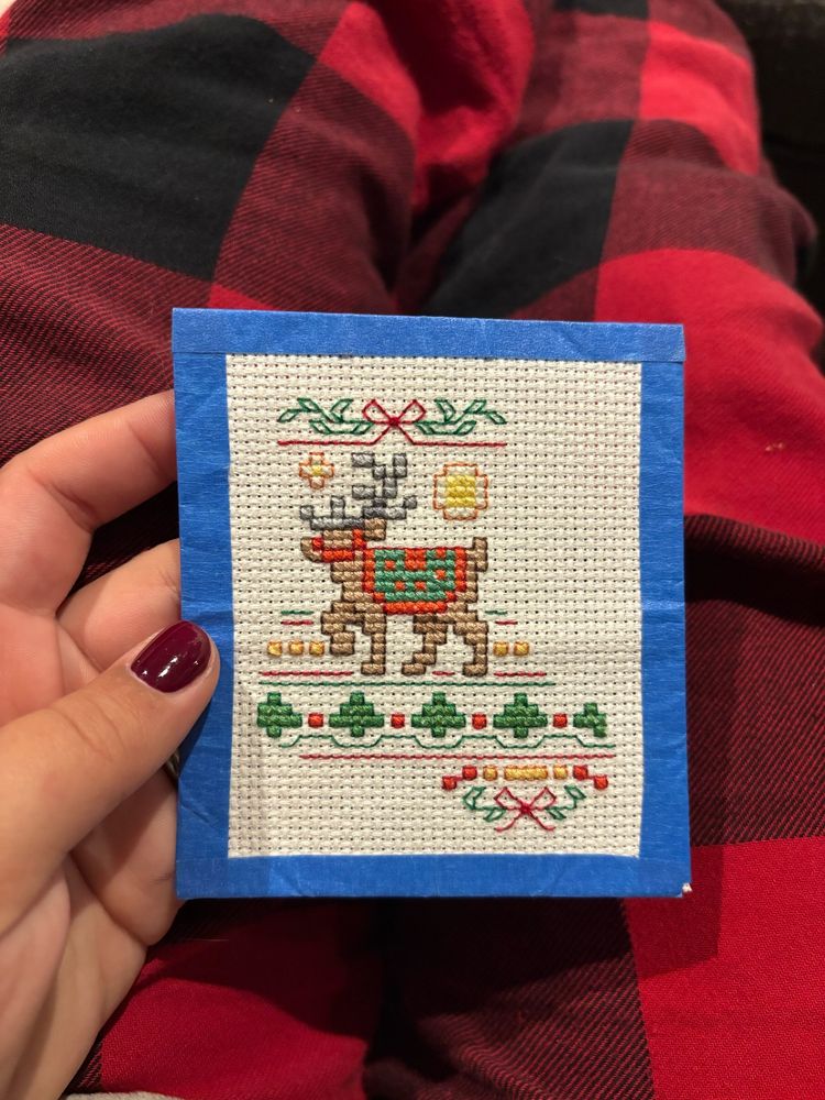 A small embroidered reindeer with embellishment in the shape of a Christmas stocking. 