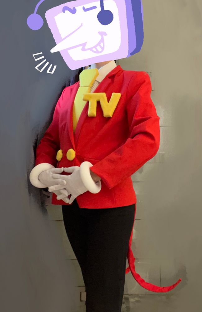 an photo of OP wearing a work in progress cosplay of Tenna from deltarune consisting of a red blazer with yellow buttons, a big yellow tie, a white dress shirt, black slacks, and white gloves. There is a large pin on the jacket that says TV. OP has their hands clasped and one leg crossed in front of the other.