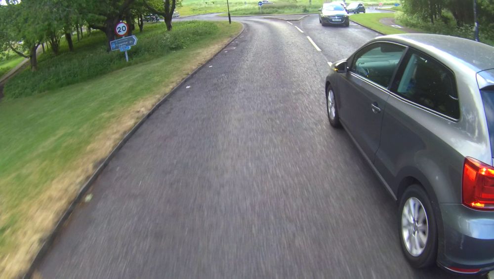 The driver is now indicating left, while driving towards oncoming traffic on the wrong side of the road, approaching a roundabout.