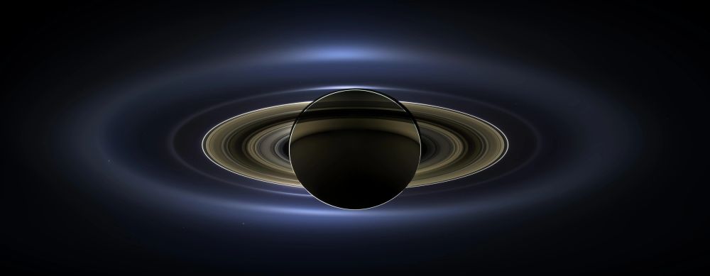 Backlit photo of Saturn, showing the dense inner rings and fuzzier outer rings against the black of space. Taken by the Cassini spacecraft while in orbit around the gas giant planet.