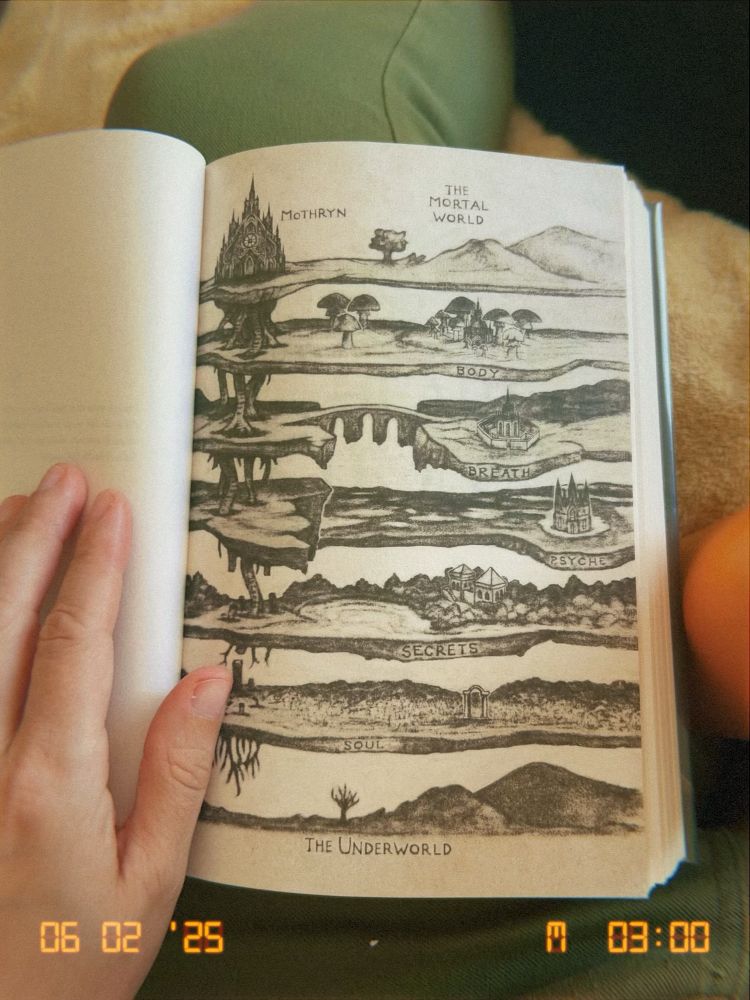 my hand holding open a book showing an illustrated map to the Underworld from the book The Songbird and the Heart of Stone by Carissa Broadbent. 