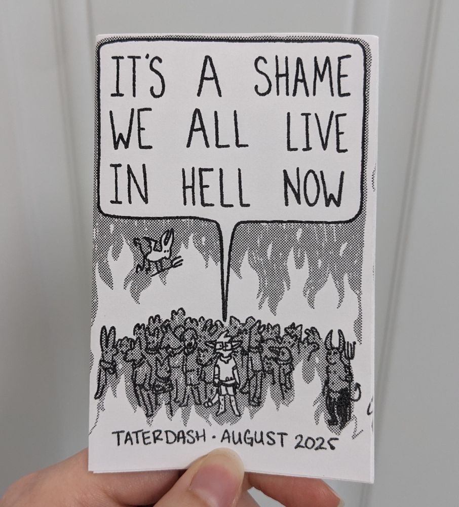 Hand holding up the cover page of a zine. It's black and white and with 50% halftones.
There's a crowd of anthro animals milling around in hell, surrounded by flames. The center shows an anthro cat saying the title:
"IT'S A SHAME WE ALL LIVE IN HELL NOW" by Taterdash in August 20215. 