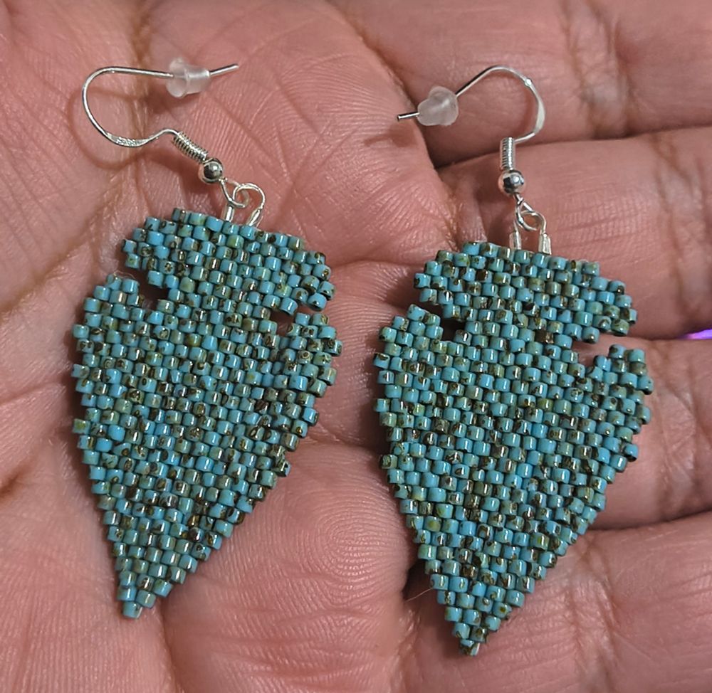 Turquoise colored brick stitch arrowhead themed earrings, silver hooks, human hand background lol