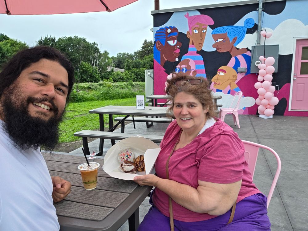 My mom and me under the umbrella at a table with donuts and a cold coffee 