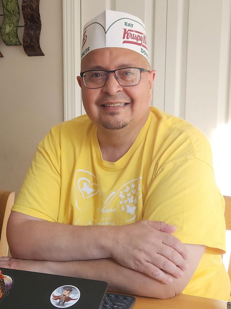 Author in a yellow t-shirt, arms crossed at a table wearing a paper Krispy Kreme hat.