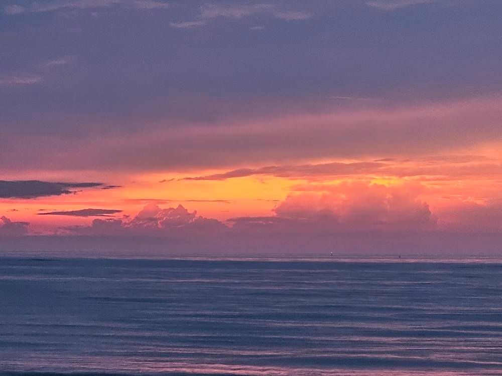 A picture taken from Siesta Key on the gulf side of Florida, looking west to the setting sun, with a storm brewing and orange, yellow tones mixed with blue and gray.