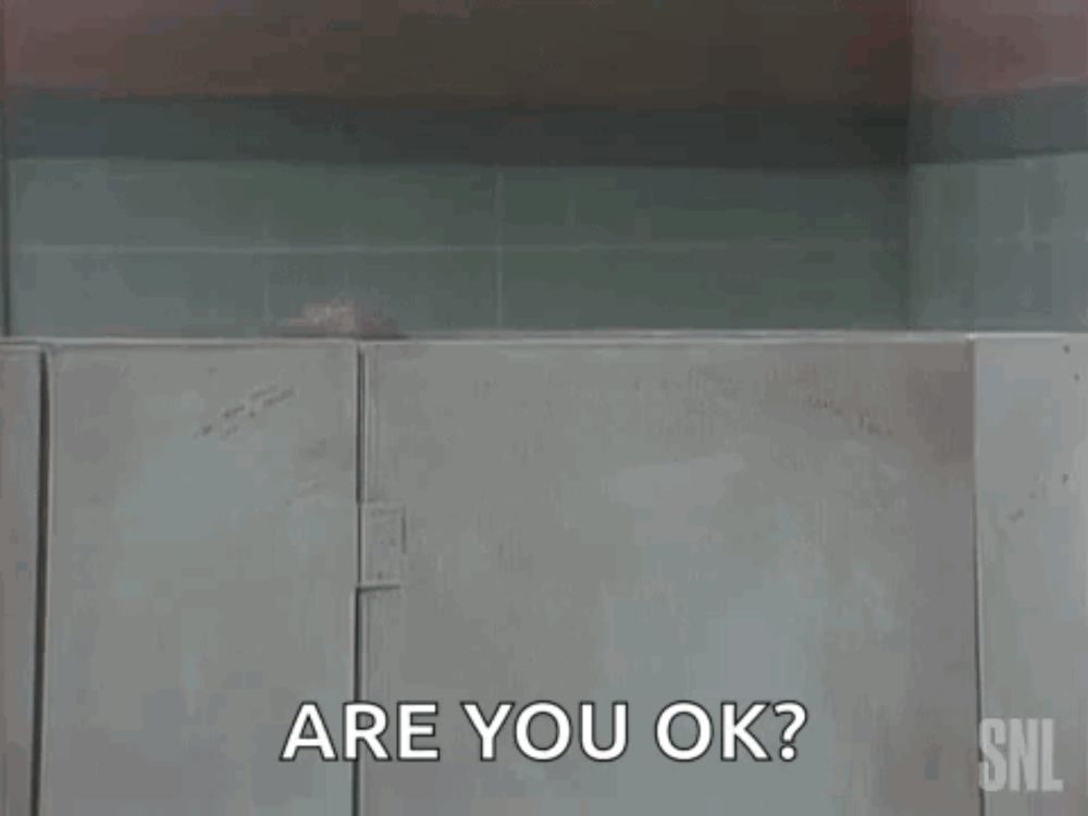 a man is peeking out from behind a wall in a bathroom and asking are you ok .