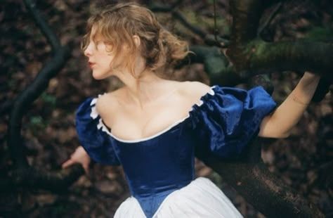 Woman in a forest and blue and white ballgown poses among the branches