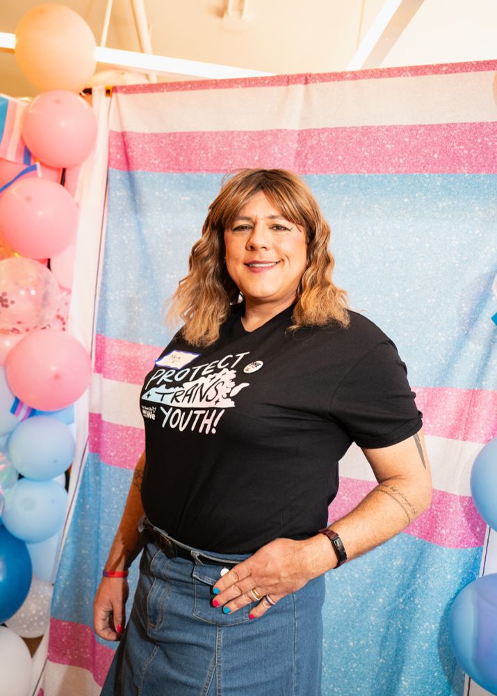 A woman smiles in front of a trans flag
