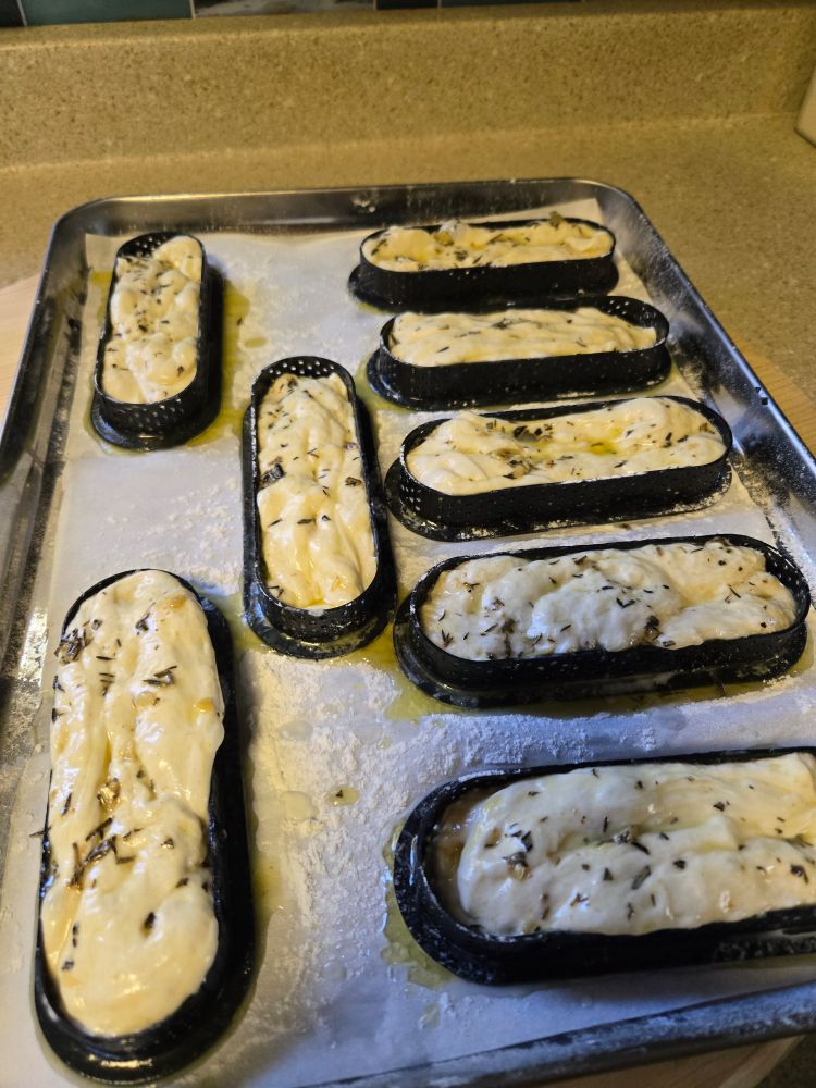 Raw herded and buttered dough in breadstick molds on a tray.