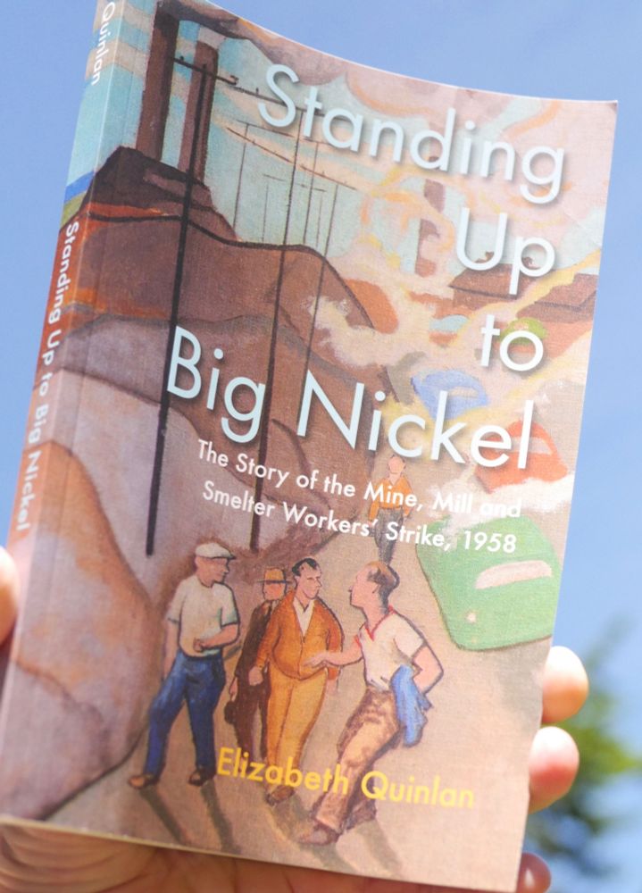 Cover of book, Standing Up to Big Nickel, features mid-century painting of workmen standing in road with mid-century cars behind them and smokestacks in the distance. The book is held aloft by a hand against the sky. 