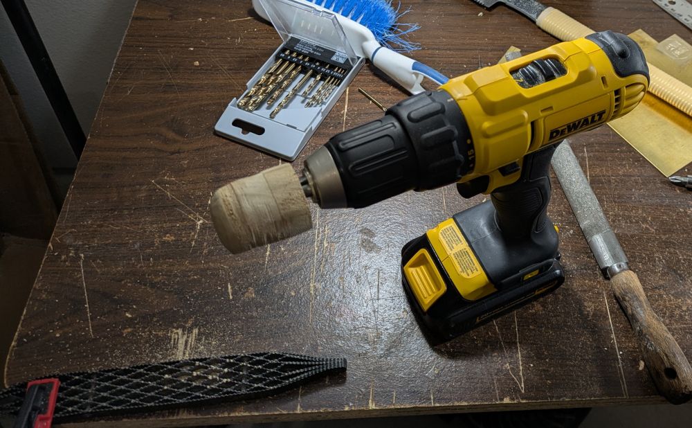 A drill with a cylinder of wood attached to it and a shinto rasp clamped to a table partially off-screen.  Spin the wood, press against rasp, out comes rounded wood cylinder.