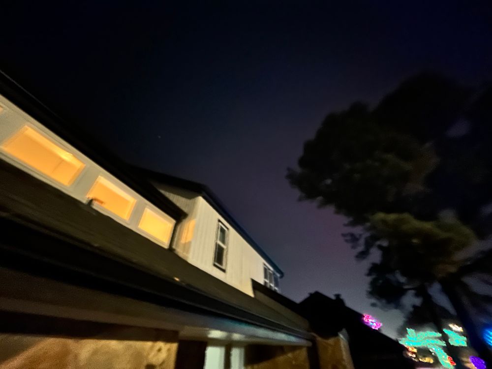 The front of my white home with lit windows with a faint red-purple glow in the sky behind a silhouetted tree. 