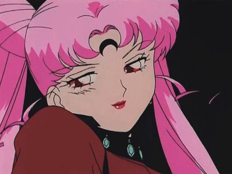 A picture of Chibiusa as Black Lady from Sailor Moon. She is also referred as Dark Lady in certain translations. 

She has a red shirt with a black collar on. It has blue jewels. Her hair is pink, her eyes are red, and she has a black moon on her forehead. She is smirking and slightly tilting her head seen as slightly below her. The background is black. 