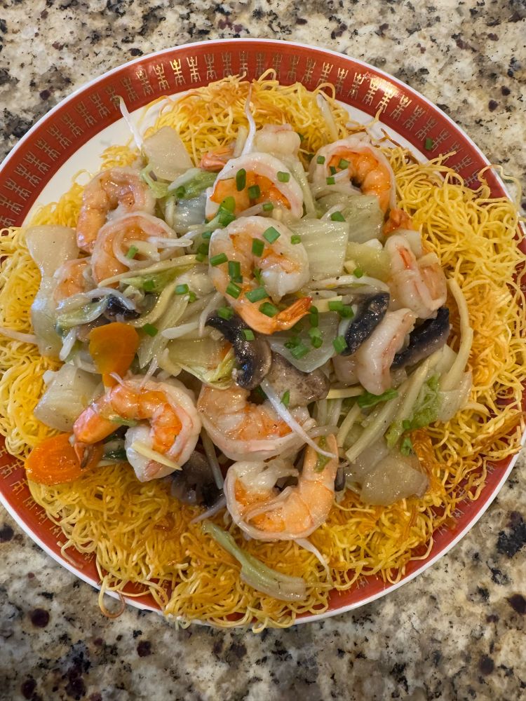 Pan fried noodles with shrimp and veggies on a round dish. 