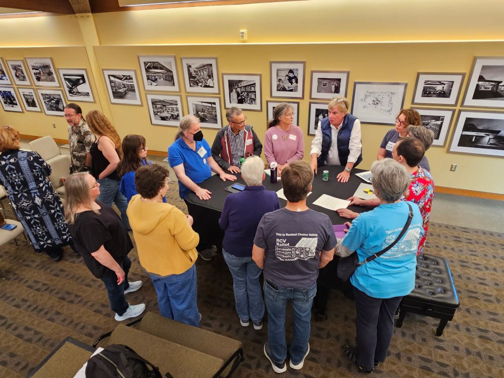 Rank MI Vote volunteers prepare to run the petition program to bring Ranked Choice Voting to Michigan through ballot initiative amendment to the state constitution in 2026. 16 volunteers are here around a piano in Oakland County.