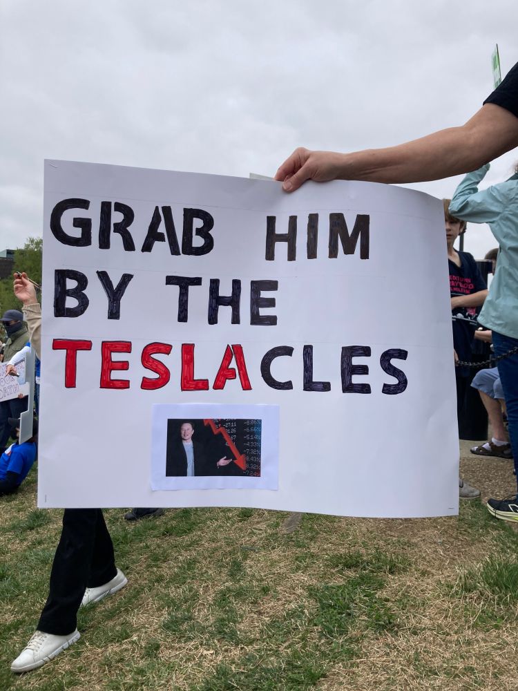 A poster board sign reads “grab him my the teslacles”