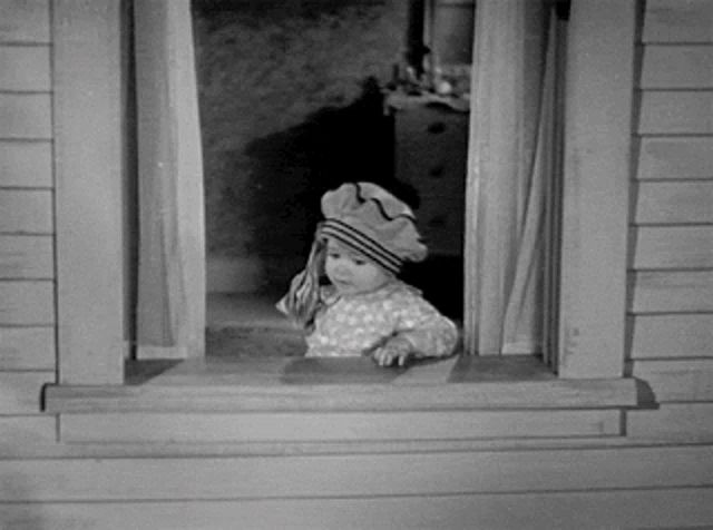 a baby wearing a hat looks out a window