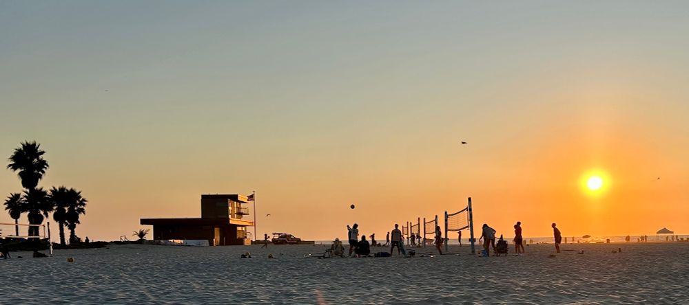 Volleyball game, palm tree, lifeguard station on the beach, back-illuminated by the setting sun.