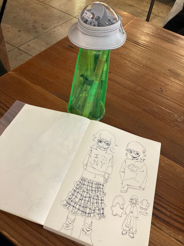 photo of another sketchbook page featuring a new OC.  my alien ship pencil case stands above it