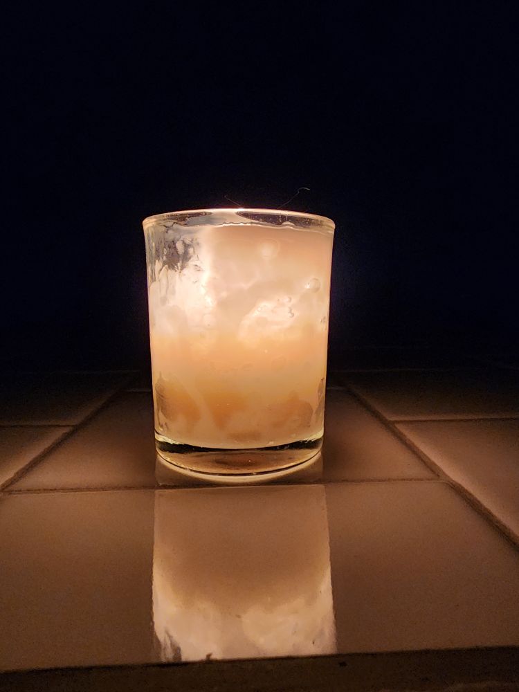 Burning white candle in a glass container. Photo taken in the dark, so the flame shines brightly. Candle will shine for over 24 hours. 